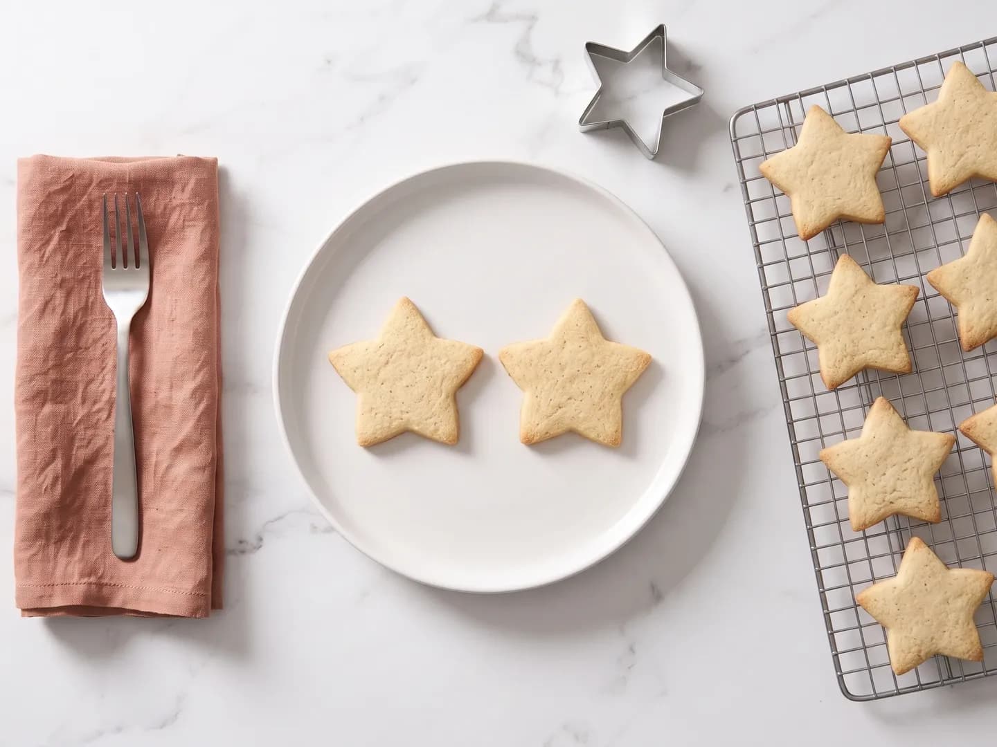 Plate of star-shaped Christmas cookies beside a cooling rack of more cookies, seen from above