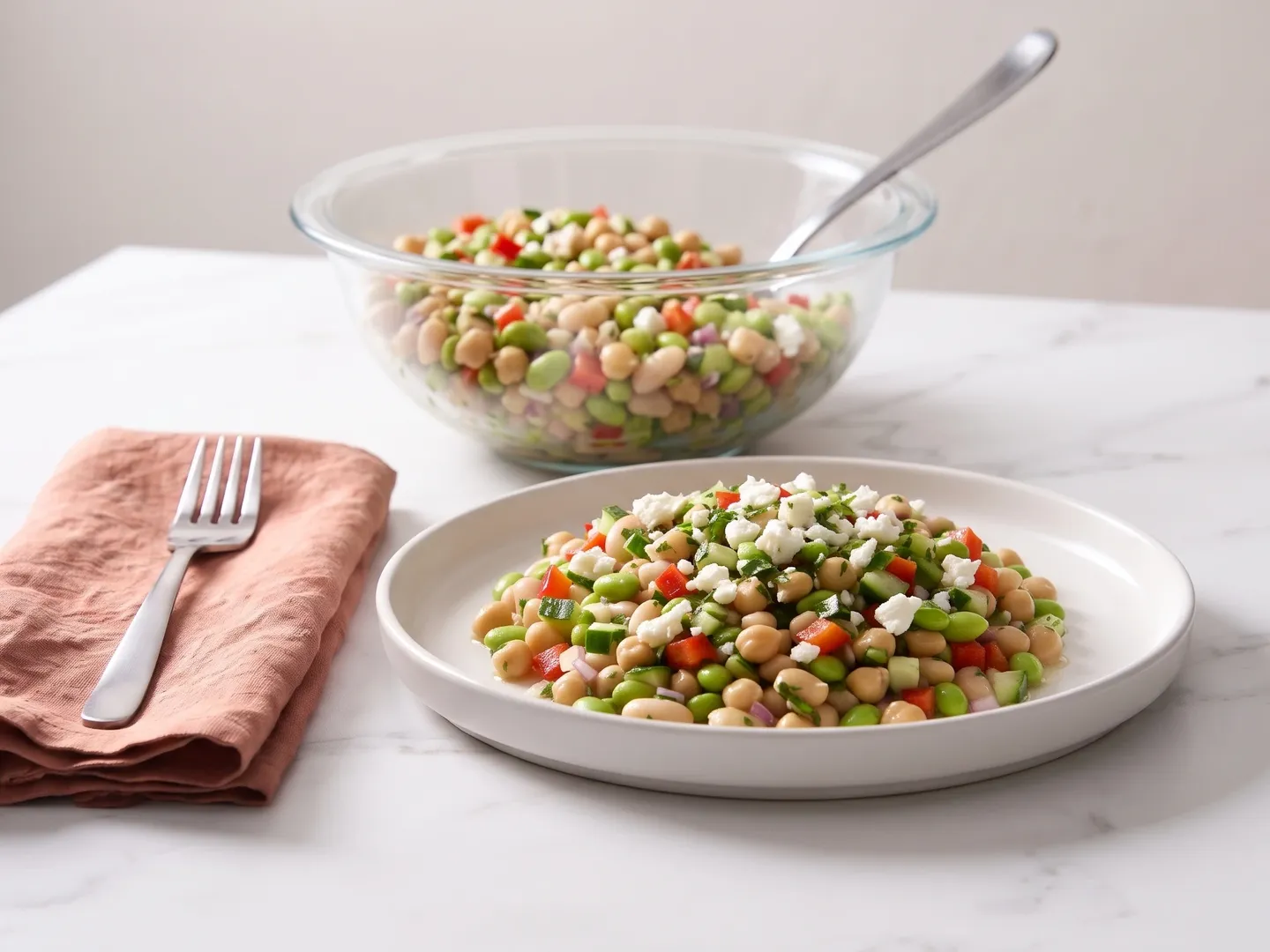 Dense bean salad on a plate with a glass bowl of salad behind