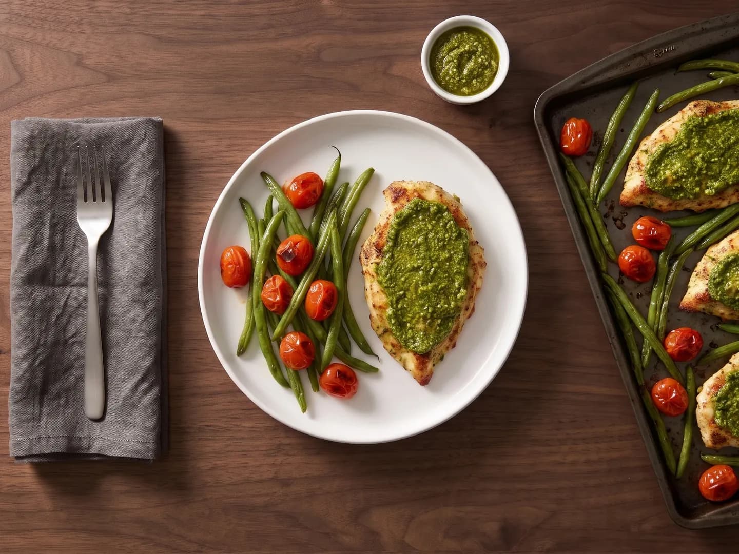 Pesto chicken on a plate beside the sheet pan, seen from above